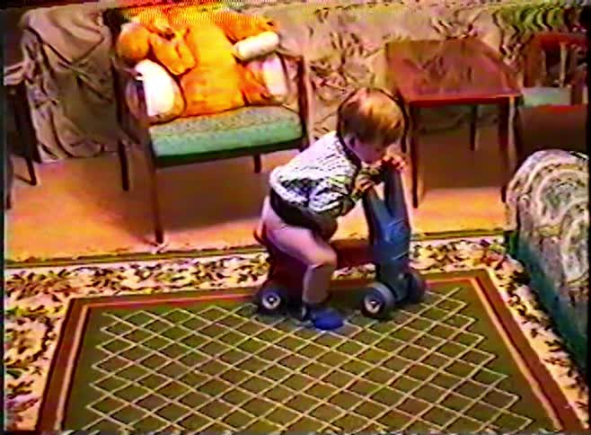 Nostalgic VHS footage of a little boy riding a toy scooter and playing with a toy vacuum cleaner at home