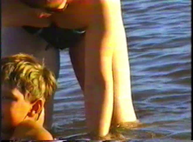 Mother helps two young children balance on a small float while playing in shallow lake water on a sunny day