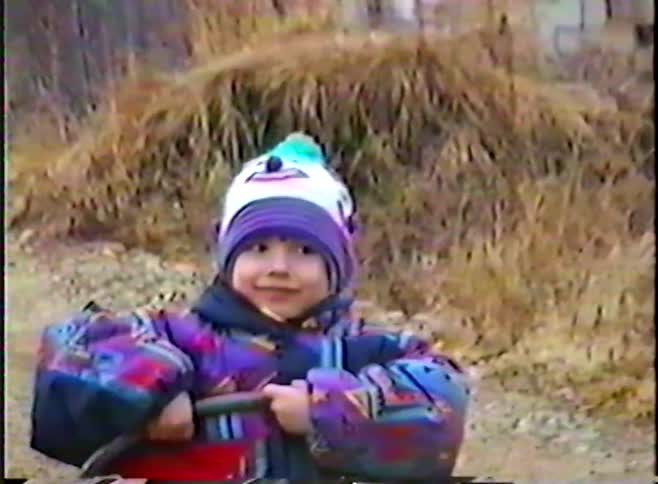 Adorable little girl bundled up in winter clothes smiles for the camera while playing with a vintage toy cart on a rural dirt road