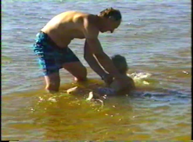 Slow-motion archival footage of a father teaching his son how to swim in a lake