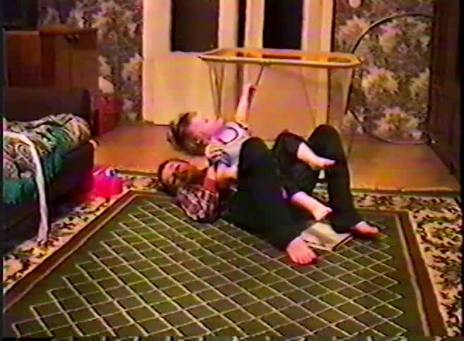 Vintage VHS footage shows two young siblings playfully wrestling and laughing on the floor at home