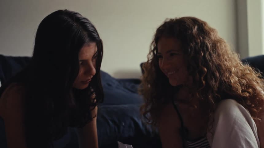 An intimate moment between two diverse female friends as they smile and laugh in a cozy room