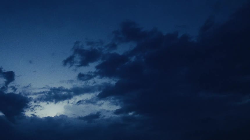 Dark, gloomy clouds slowly pass by in the deep blue sky at twilight