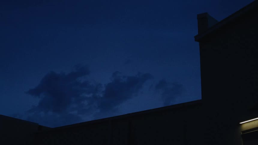 Dark clouds float across the deep blue night sky over the silhouette of a building