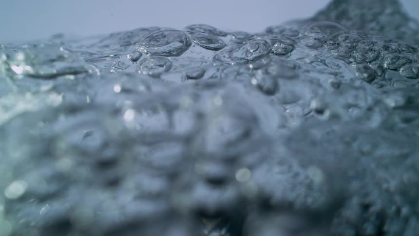 Clear water surface boils and bubbles in slow motion, followed by an underwater perspective of air bubbles floating up