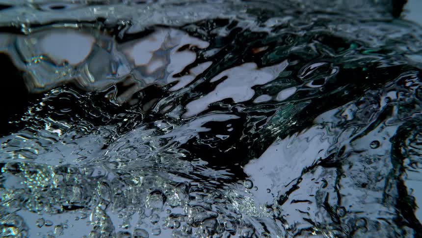 An underwater slow motion view shows clear water swirling and bubbling against a light background