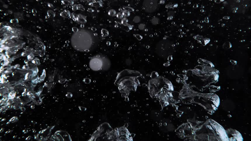 Clear bubbles of air rise chaotically in slow motion against a solid black background