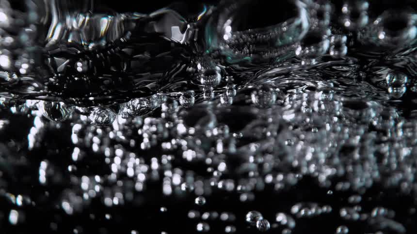 A mesmerizing slow-motion macro view of clear water bubbling intensely against a stark black background