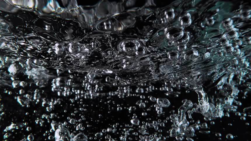 An abstract slow-motion close-up of turbulent water and air bubbles churning against a black background