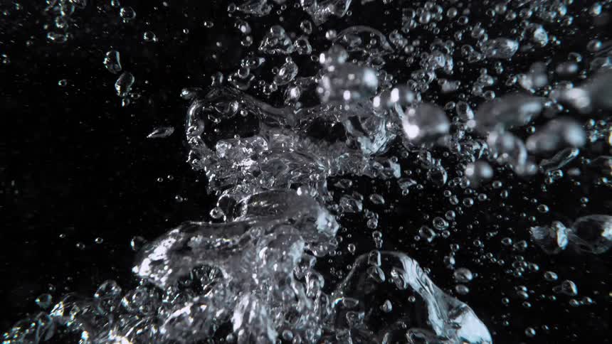 Chaotic air bubbles rise through dark water in a mesmerizing slow-motion close-up shot