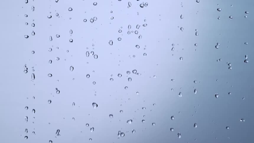 Slow motion video of raindrops falling against a clean, light blue background creating a soothing and mesmerizing effect