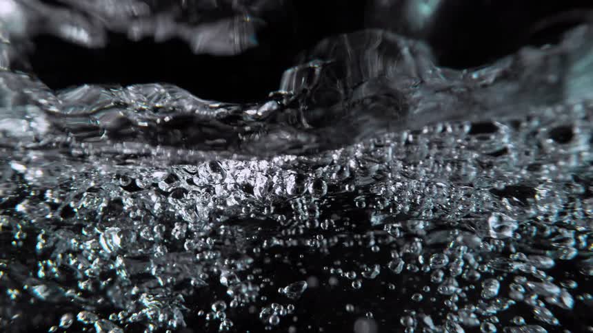 An abstract, super slow-motion close-up captures the chaotic turbulence of water and bubbles from an underwater perspective against a black background