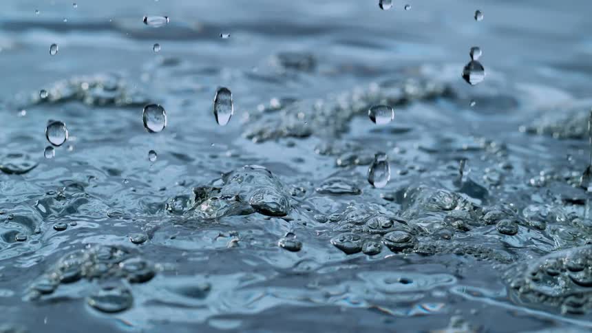 Mesmerizing slow-motion close-up of water droplets falling and splashing into a rippling blue surface