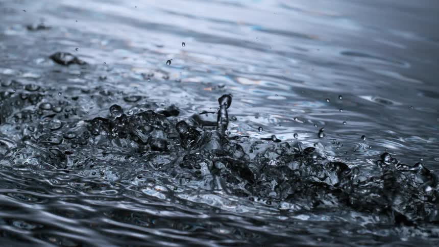 A dramatic close-up of turbulent dark water flowing and splashing in super slow motion