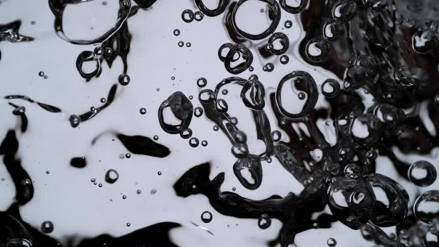A super slow-motion macro shot of clear bubbles rising and morphing in turbulent water against a high-contrast background