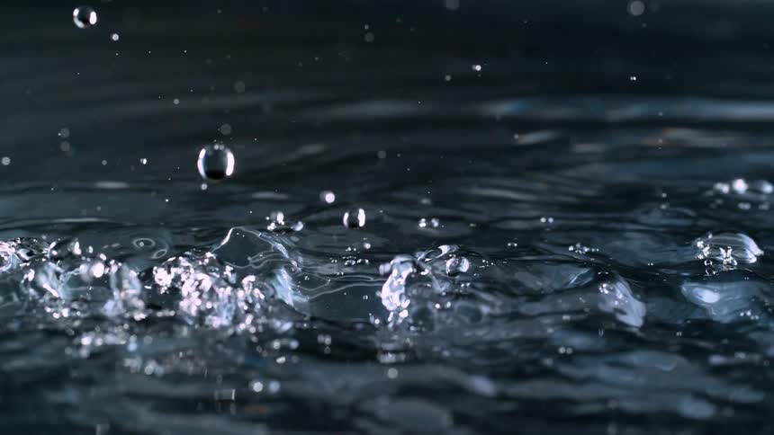 A dramatic close-up of water droplets falling and splashing in super slow motion against a dark background