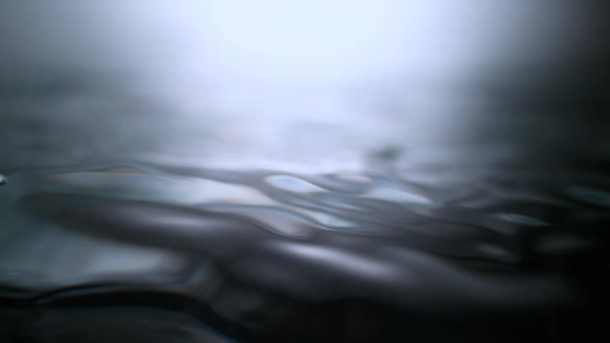 Ethereal slow-motion macro shot of a silver liquid surface undulating, with soft ripples and bubbles forming