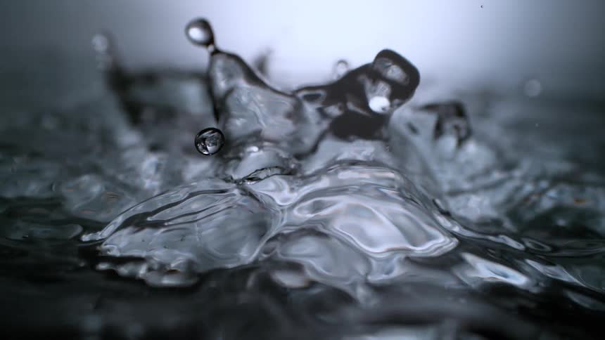 A dramatic super slow-motion macro shot of water droplets falling into dark water, creating beautiful ripples and splashes