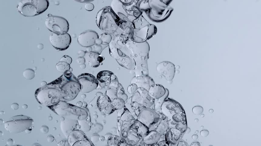 Slow motion macro shot of clear viscous gel being poured into water, creating beautiful abstract bubbles and formations