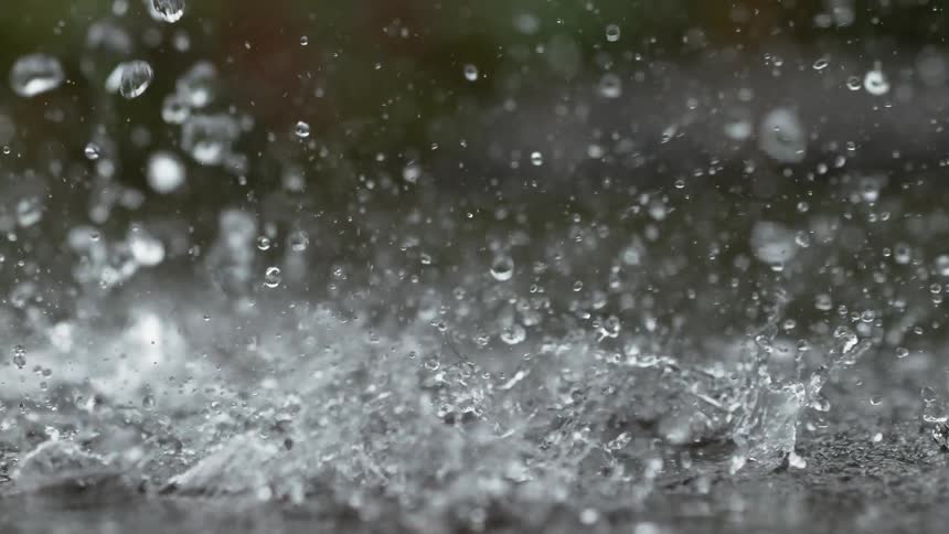 Heavy raindrops create mesmerizing splashes and ripples as they hit the pavement in super slow motion