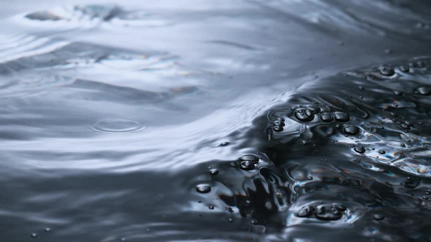 Gentle waves and bubbles ripple across a dark water surface in a mesmerizing slow-motion closeup