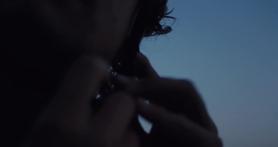 A silhouetted cyclist with a mustache fastens his helmet strap against a dark blue twilight sky