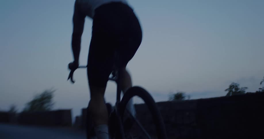 A determined male road cyclist in full gear trains hard on a secluded, winding road during the quiet twilight hours