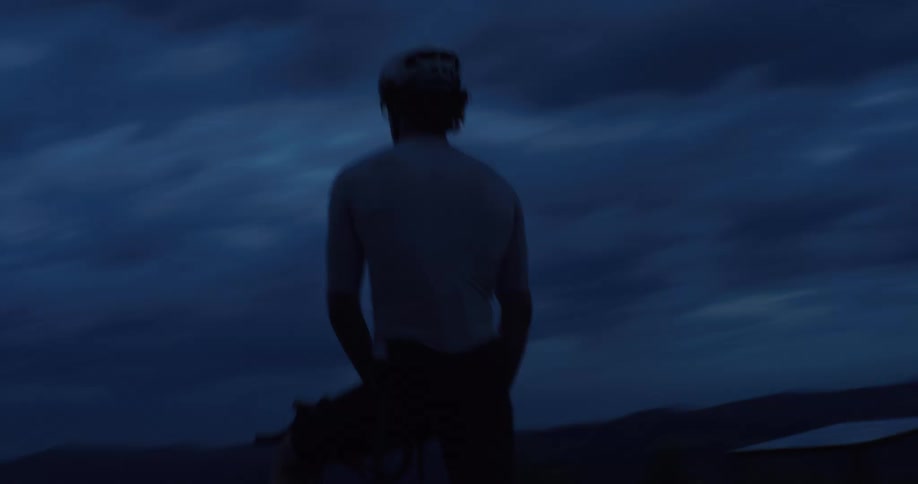 A silhouetted cyclist rides his road bike at twilight, set against a dramatic and moody cloudy sky
