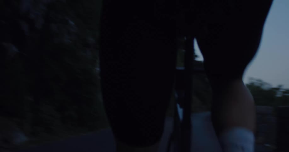 Handheld close-up of a professional cyclist training on a winding mountain road at dusk