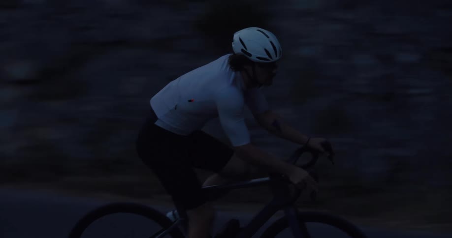A focused male athlete cycles intensely along a dark road in the evening