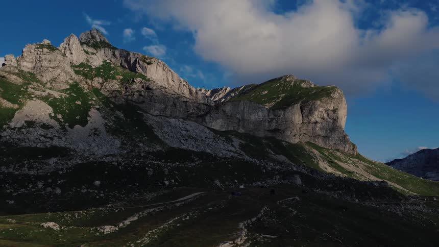 Sunlight hits the peaks of a dramatic mountain range with lush green slopes and shadowed valleys