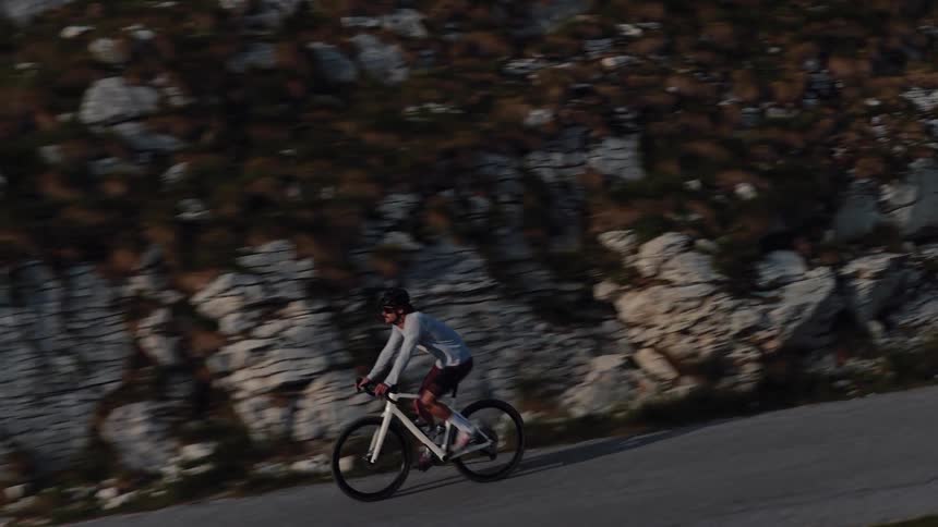 A determined cyclist wearing a helmet and athletic gear rides a road bike up a steep, winding mountain pass at sunrise