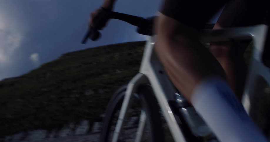 Dynamic close-up of a cyclist's legs and wheels as they pedal vigorously up a steep gravel mountain pass at twilight