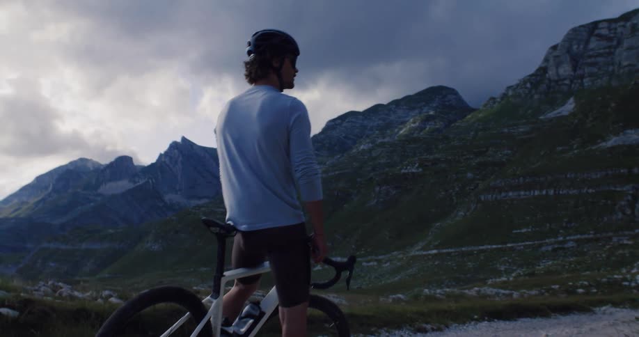A male cyclist takes a break on a remote mountain road to admire the dramatic, expansive landscape