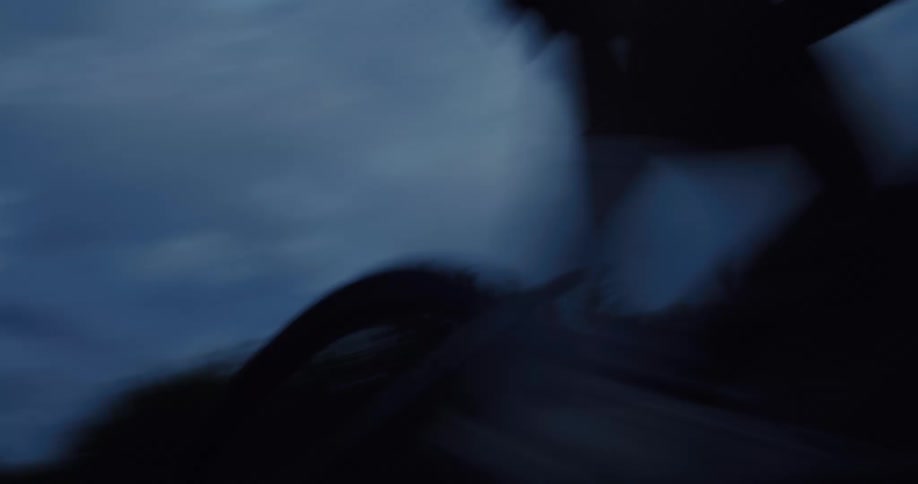 Low-angle shot of a cyclist speeding past the camera on a dark road during twilight