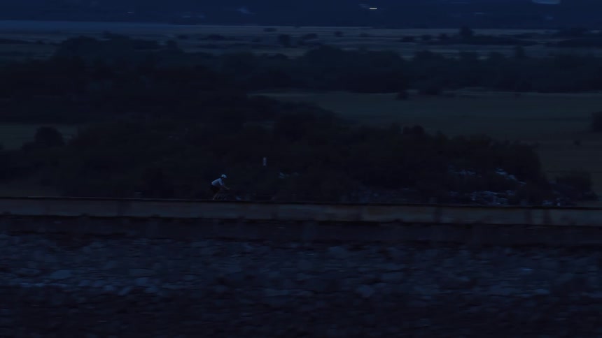 A lone cyclist rides along a country road in the dark blue light of dusk