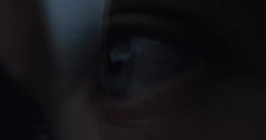 The pupil of a person's eye dilates and reflects light while watching something intently in the dark