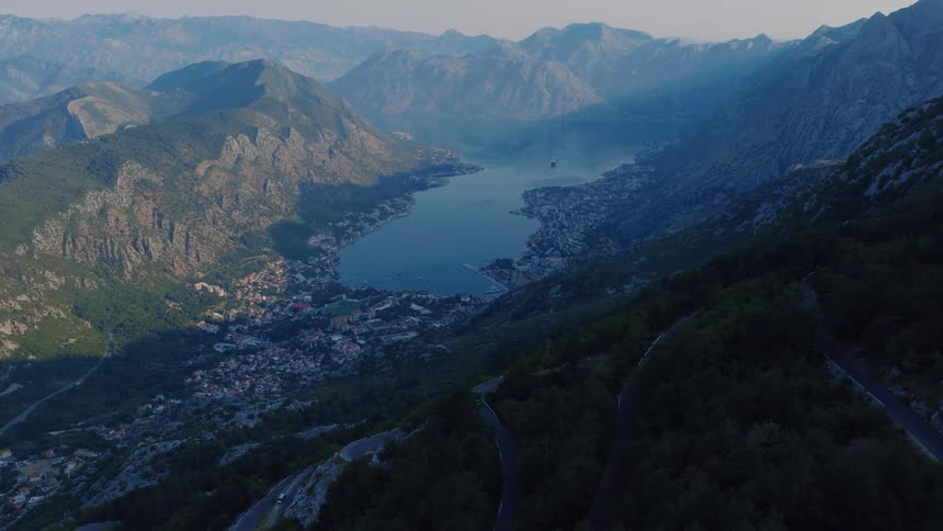 Breathtaking aerial pan over the winding mountain roads overlooking the beautiful Bay of Kotor in Montenegro during a hazy sunrise