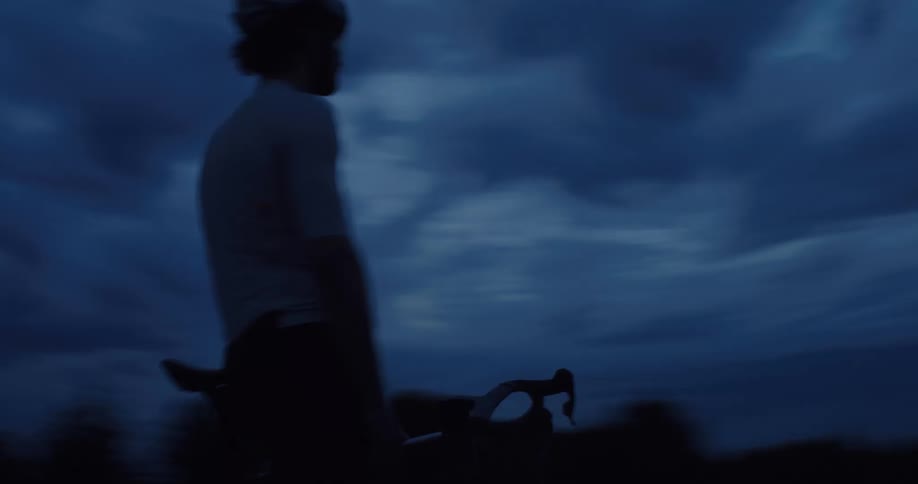 Side tracking shot of a male cyclist riding his bike under a dark and moody sky at dusk