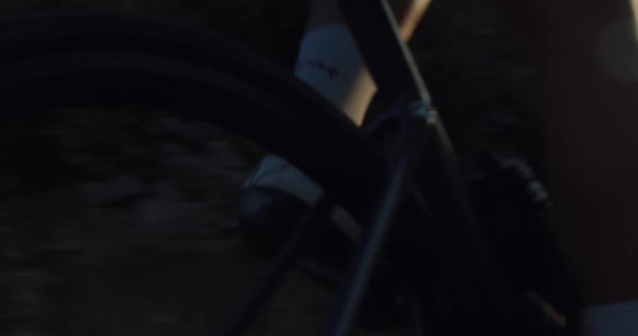 Close-up slow-motion shot of a professional cyclist's legs pedaling a bike with a strong sun flare in the background