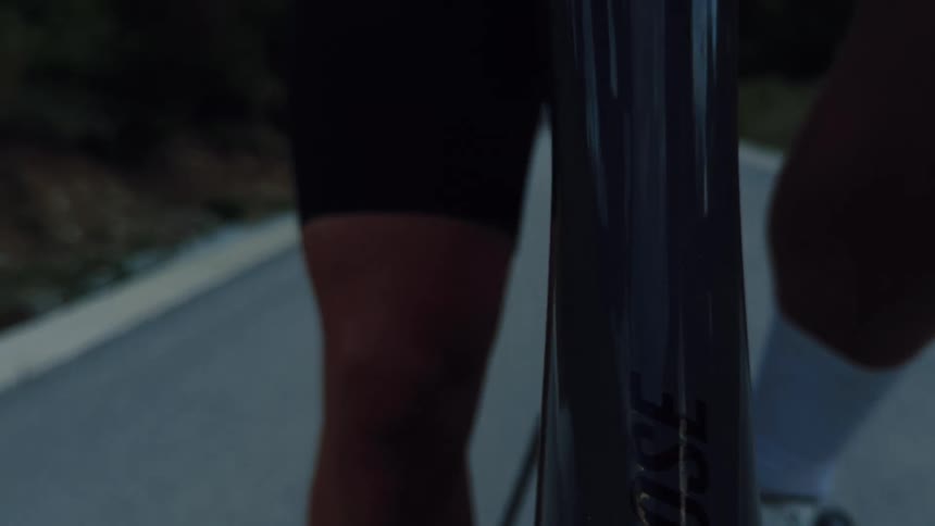Close-up shot of a cyclist's legs as they pedal a road bike along an asphalt road at dusk