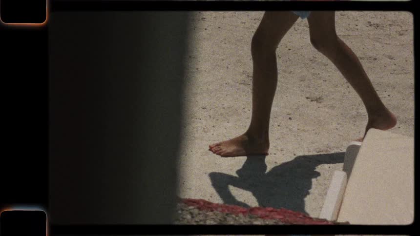 Super 8 vintage footage captures the bare feet of a person walking on the sand on a sunny day