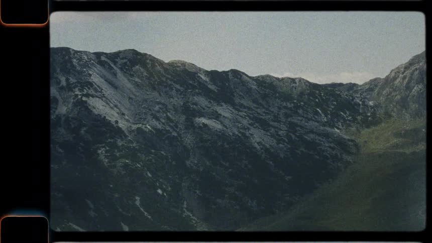 Vintage 8mm footage zooms out from a rugged mountain peak to reveal a vast green valley landscape