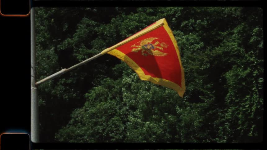 A vintage film shot captures the national flag of Montenegro waving proudly against a backdrop of dense green trees