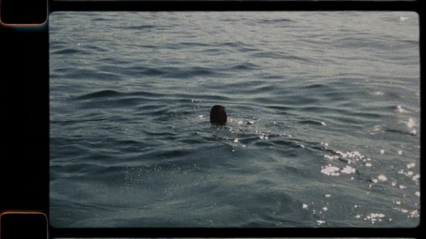 Vintage Super 8 film captures a man in slow motion as he leaps joyfully off a stone pier into the sparkling sea