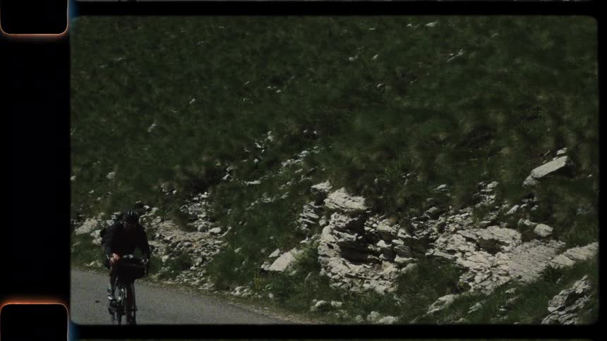 Authentic 8mm film captures a man on a bikepacking adventure, cycling up a steep and scenic mountain road