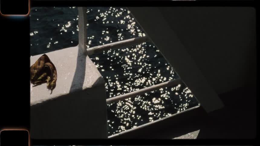 Vintage Super 8 film captures the mesmerizing sparkle of sunlight on the deep blue sea from the deck of a moving boat