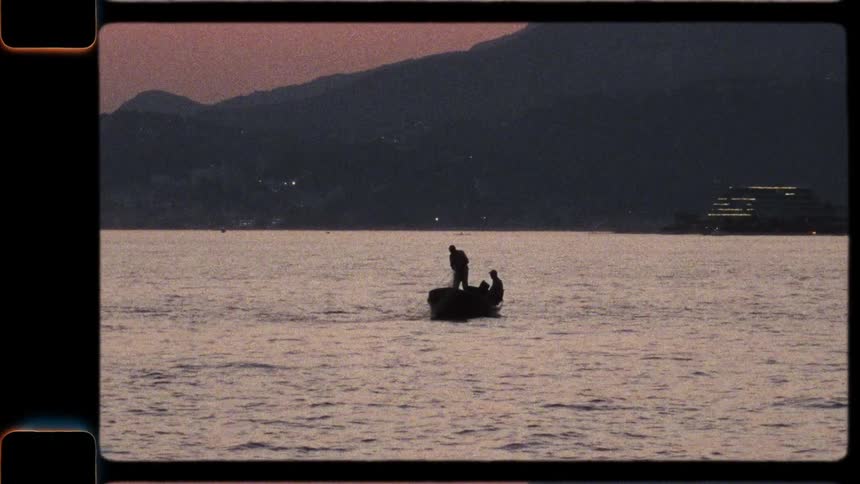Vintage 8mm film captures the silhouette of fishermen pulling in nets from a boat at dusk
