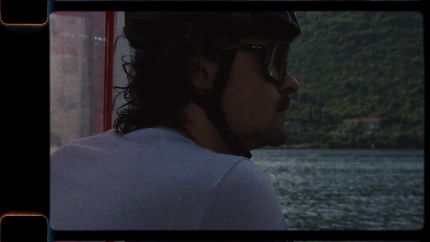 Vintage 8mm footage shows a cyclist in a helmet and sunglasses looking out over the water from a boat