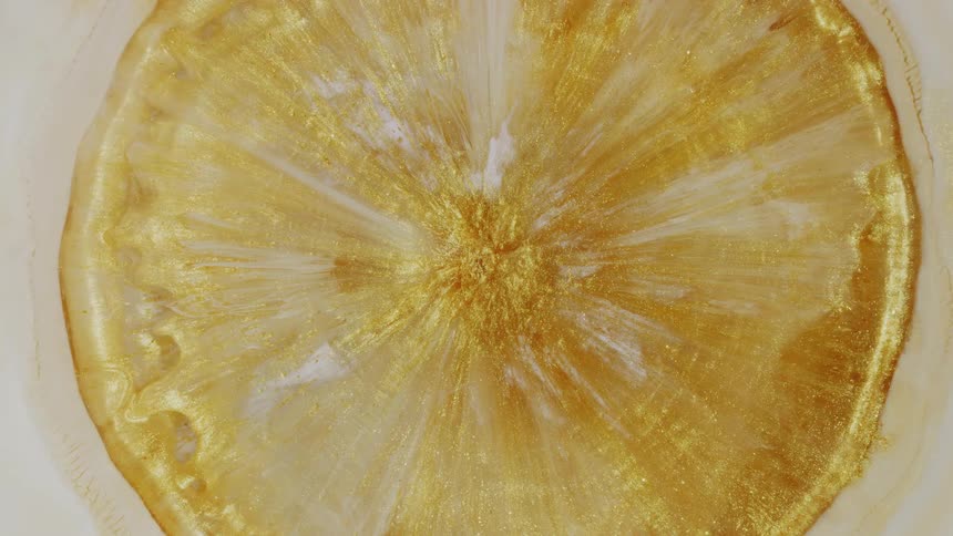 A golden orb of metallic paint with glitter expands slowly in a milky white liquid, creating a stunning abstract visual